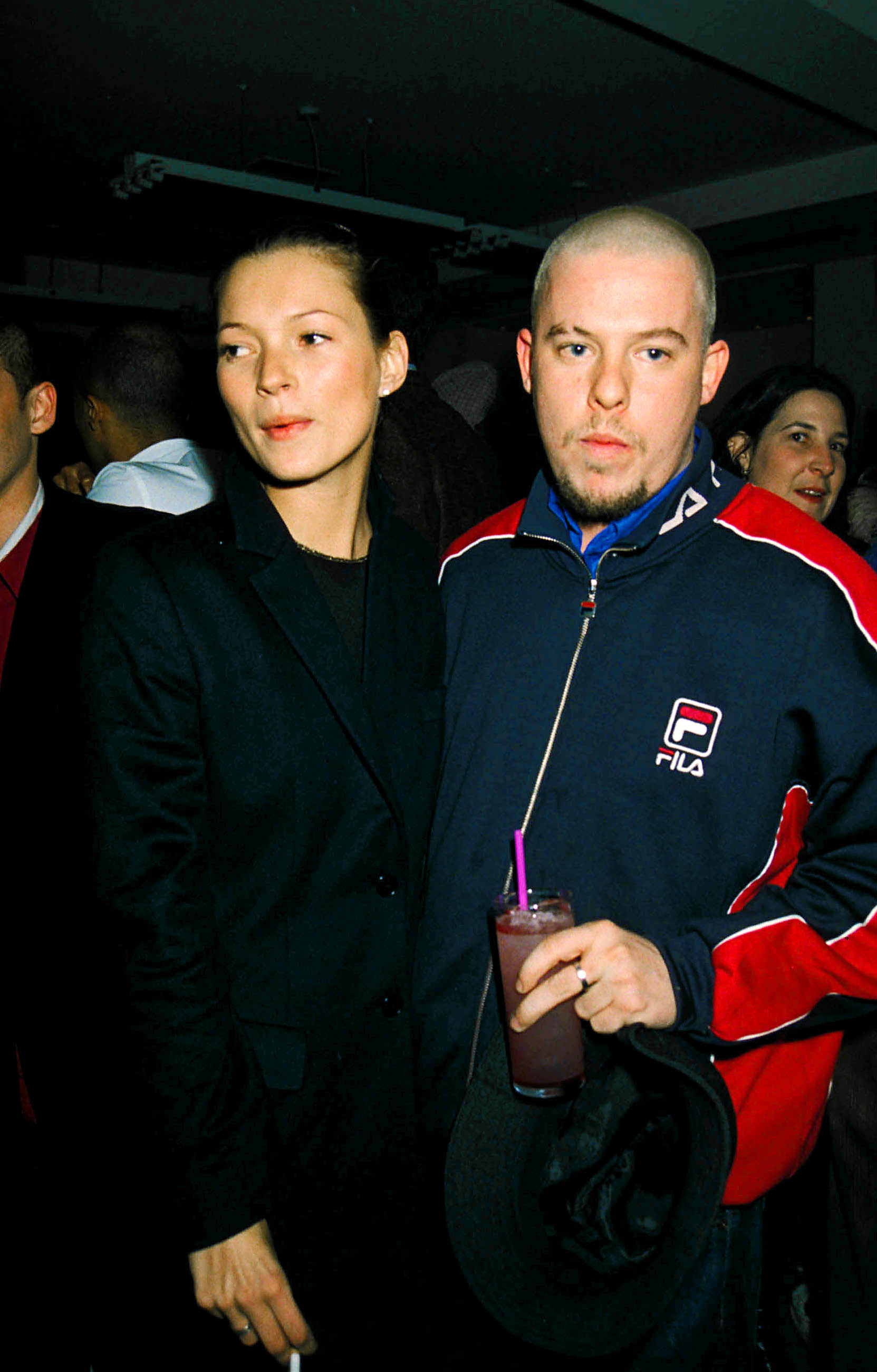 A slender white model with her hair pulled back standing close to a white man with close-shaved head and goatee.