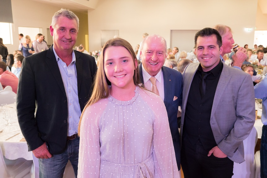 A young girl stands before three men, smiling at the camera.