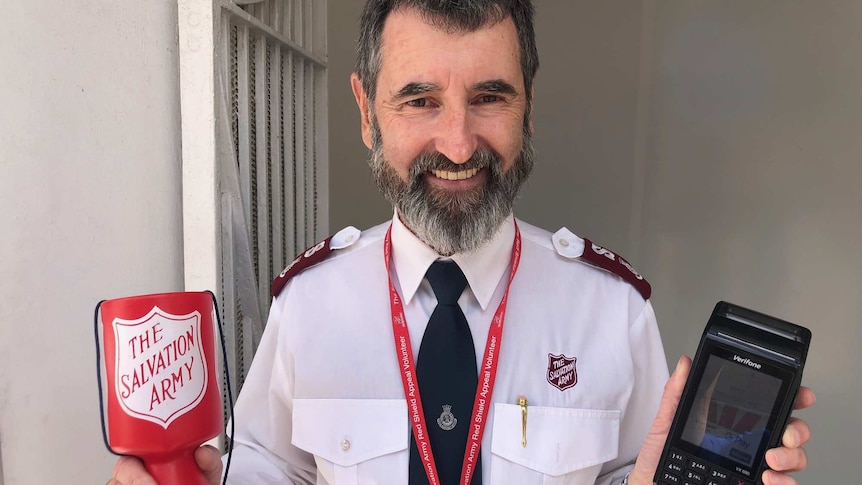 Major Paul Hateley, of the Salvation Army, holding up a cash collection container and a paypass machine