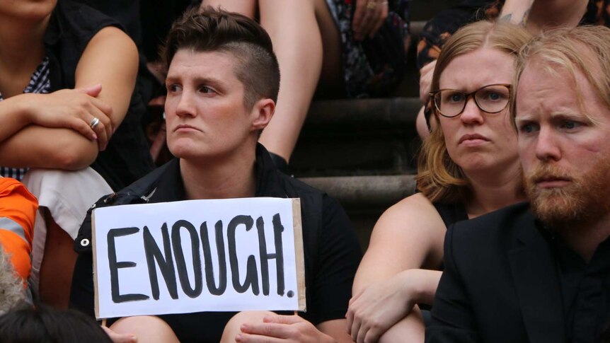 A person at the vigil holds a sign reading "ENOUGH".