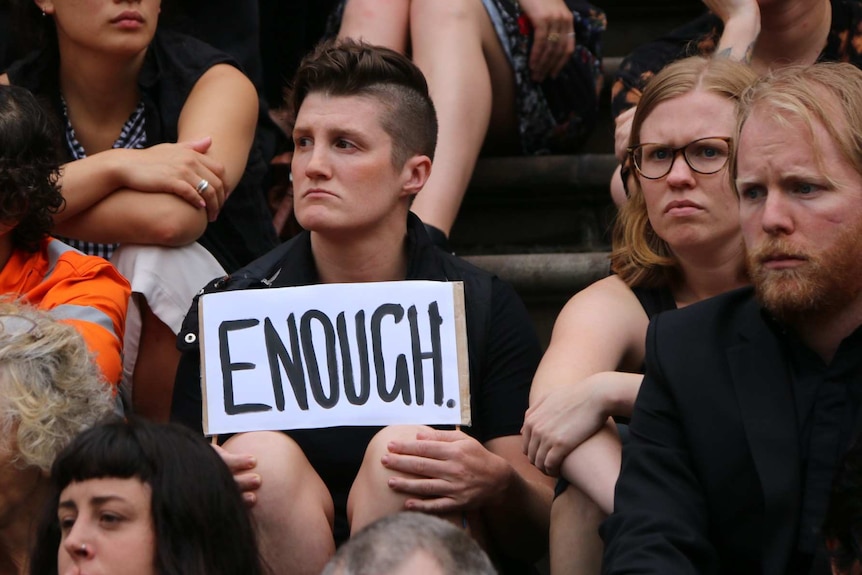 A person at the vigil holds a sign reading "ENOUGH".