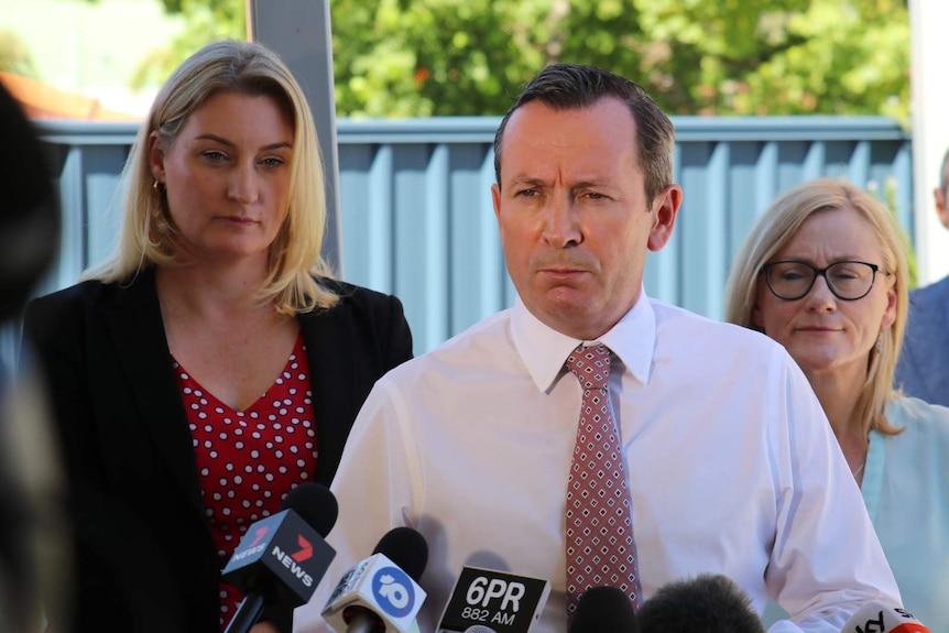 Two women stand behind Mark McGowan at a press conference