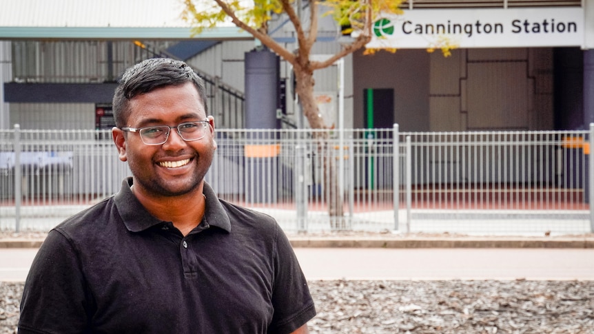 A smiling, tanned man wearing glasses and a black polo shirt. Cannington train station sign in the background.