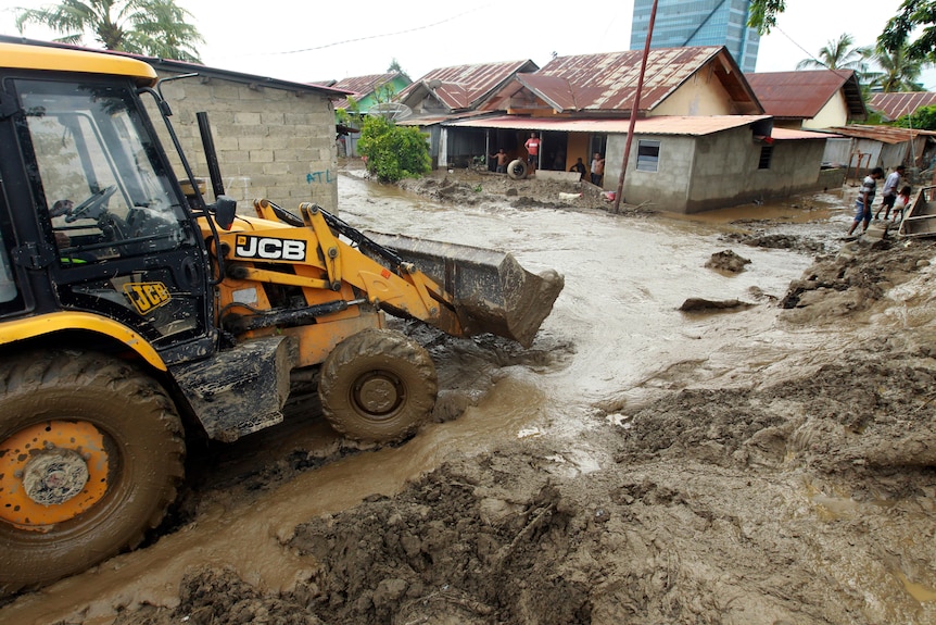 Heavy earth-moving machines lead a path between the houses through the thick brown mud left by the floods.