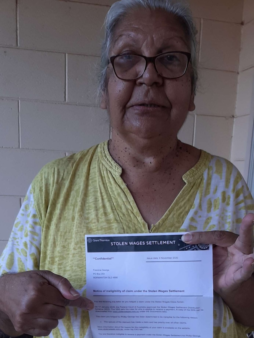 An Indigenous woman in a yellow top hold up a letter about a stolen wages entitlement.