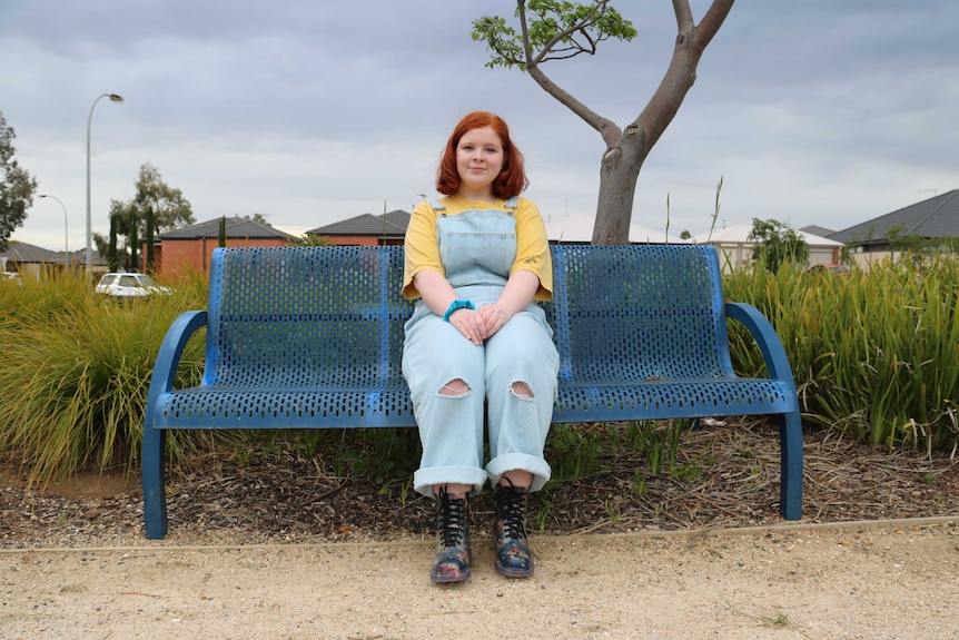 A young girl in overalls sitting on a park bench outside