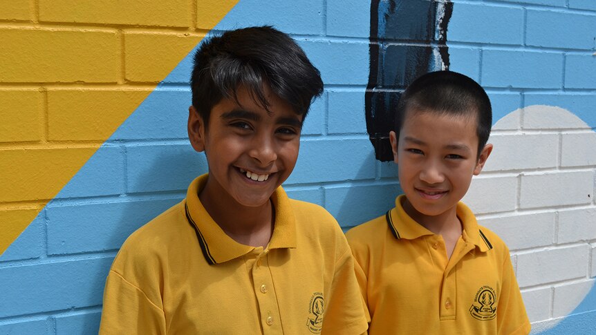 Colour photo of primary school students Mikaeel and Tony posing in front of brightly coloured mural wall.