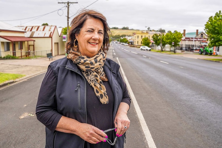 A woman with a leopard print scarf stands smiling at the camera, a pretty building-lined street behind her.