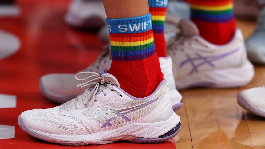 A Swifts player wears white netball shoes and long ankle socks with rainbow colours and the word SWIFTS