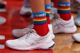 A Swifts player wears white netball shoes and long ankle socks with rainbow colours and the word SWIFTS