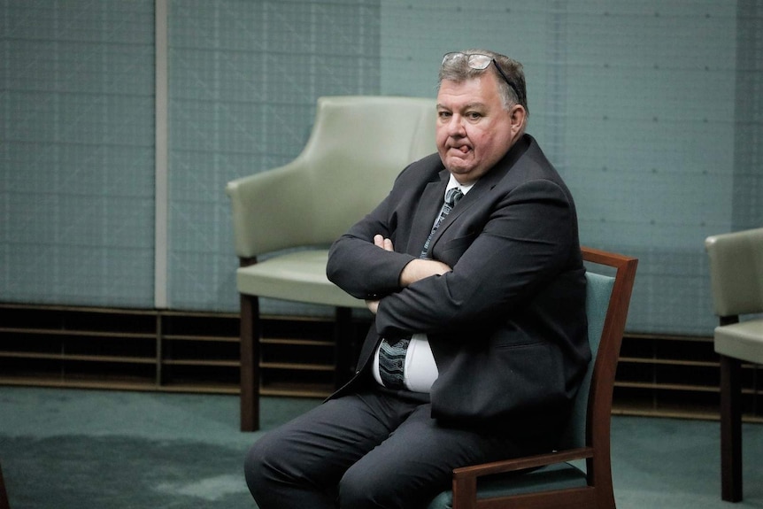 A man in a suit crosses his arms in his seat and sticks his tongue out