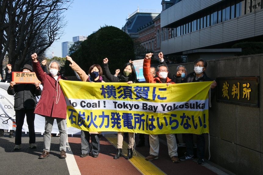 People hold a banner with Japanese writing. 