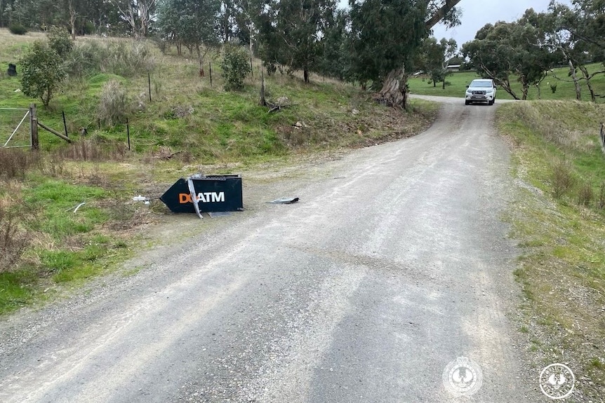 A damaged ATM on its side on the side of a road, with a car in the far background