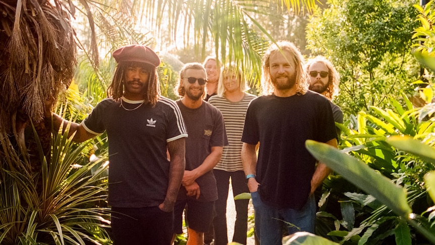 Press shot of Ocean Alley; band is standing in a botanic setting, surrounded by palms and trees