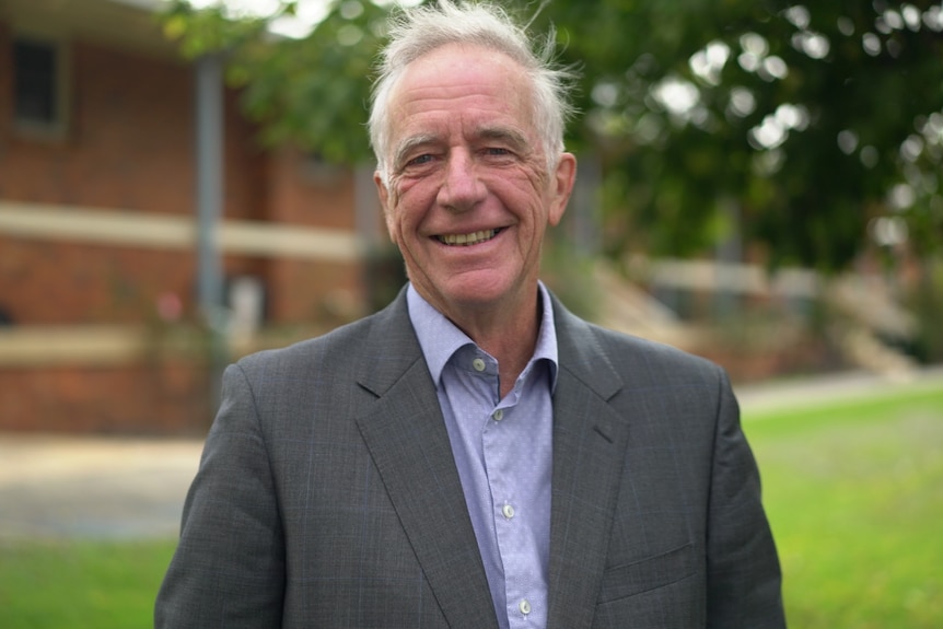 Elderly man wearing a grey suit and light blue shirt smiling.