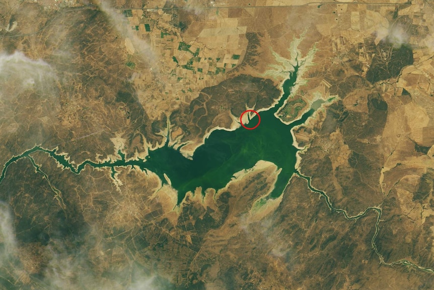A satellite image of the Valdecanas Reservoir, with brown patches of water and a wide ring of sand around the perimeter.