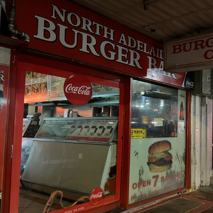 red frontage of burger shop with glass window and red soft drink advertising with tables out front