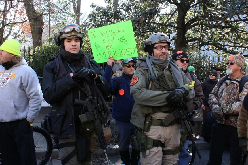two men in armour hold rifles in a group of protesters including a man holding a sign that says i will not be infringed