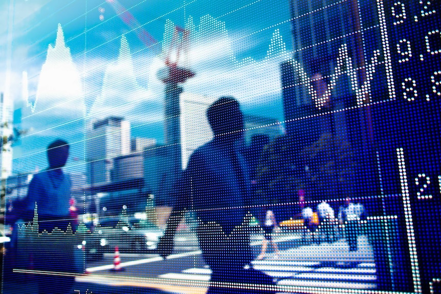 People walk past a stock market graph in a window.