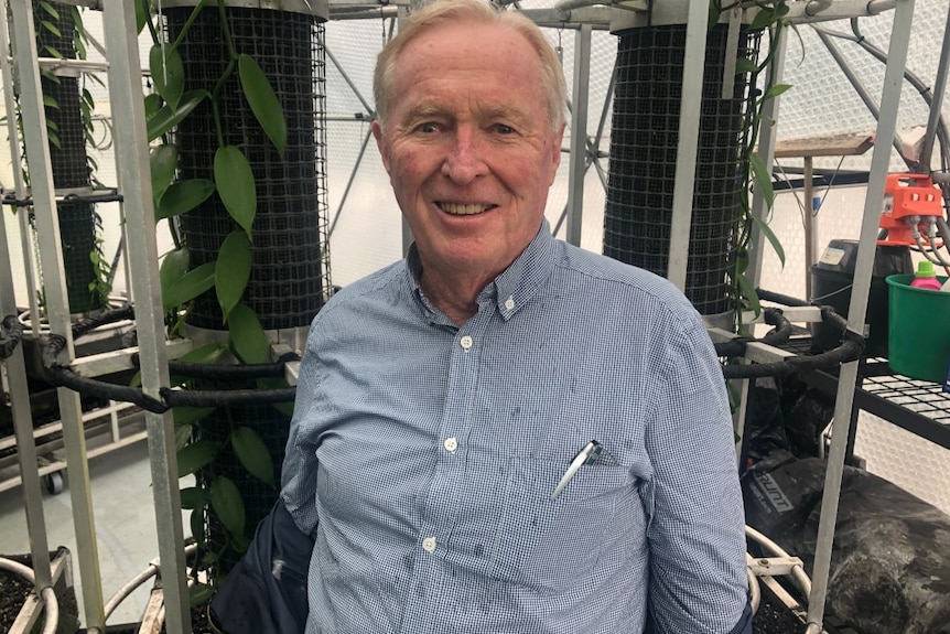 A man in a blue shirt stands in front of metal trellises, smiling.