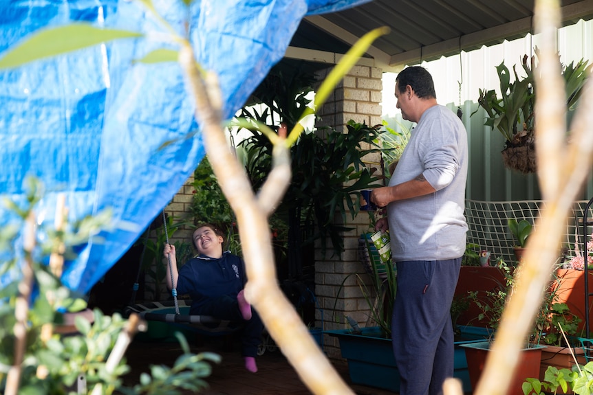 A man in a grey jumper talks to a girl who is sitting down outside. 