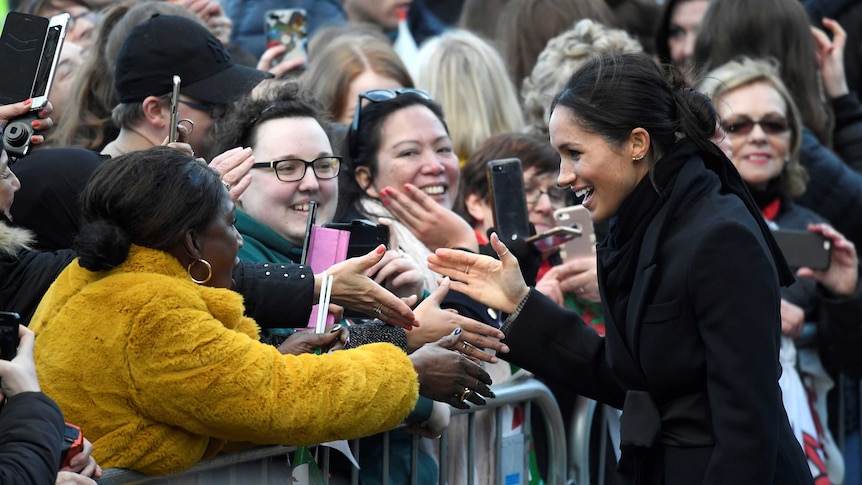 Meghan Markle talks to fans taking photos with their phones.
