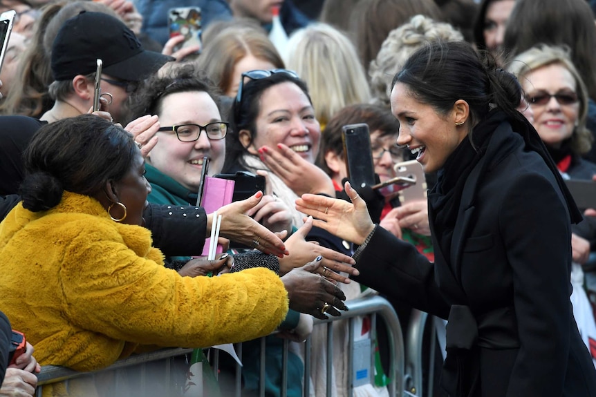 Meghan Markle talks to fans taking photos with their phones.