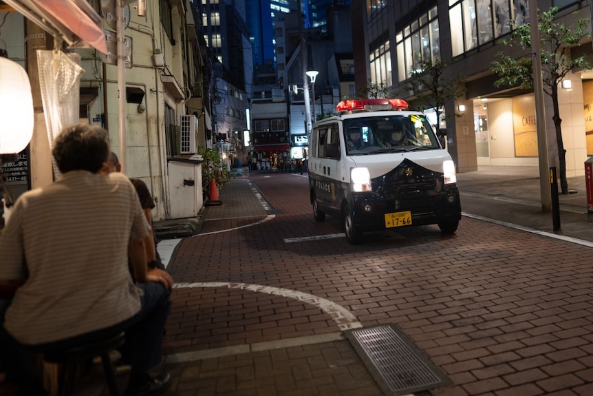 A police van drives down a Tokyo street at night 