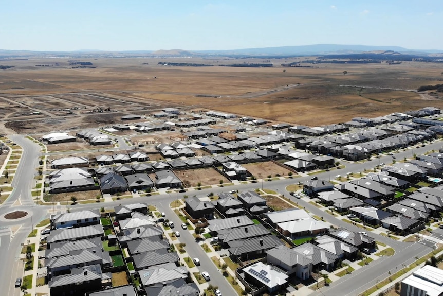A birds-eye view from a drone showing suburban housing meeting grassland.