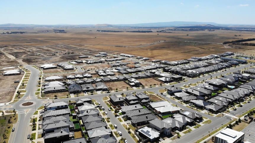 A birds-eye view from a drone showing suburban housing meeting grassland.