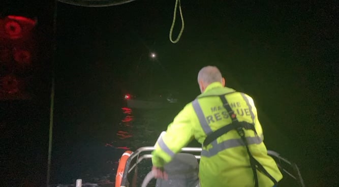 A marine rescue vessel approaches a yacht in the dark.