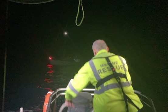 A marine rescue vessel approaches a yacht in the dark.