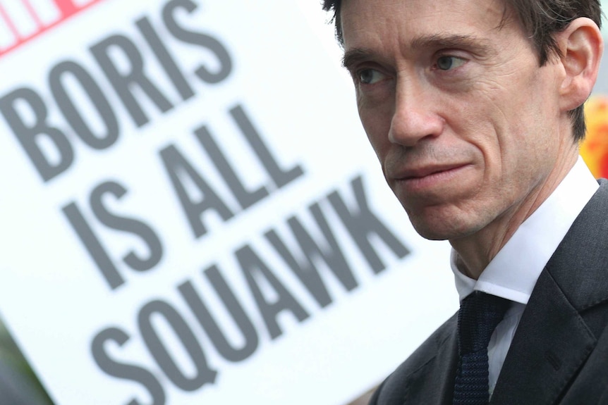 A close up of Rory Stewart with a sign in the background reading 'Boris is all squawk'.