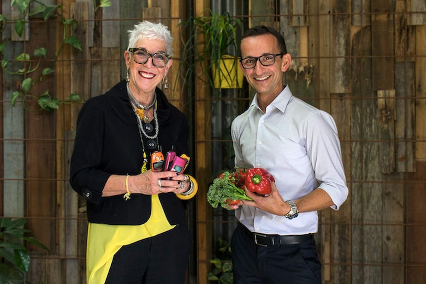 Woman holding mobile phones and man holding vegetables.