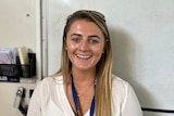 Young blonde woman smiles at camera in front of a school classroom whiteboard 
