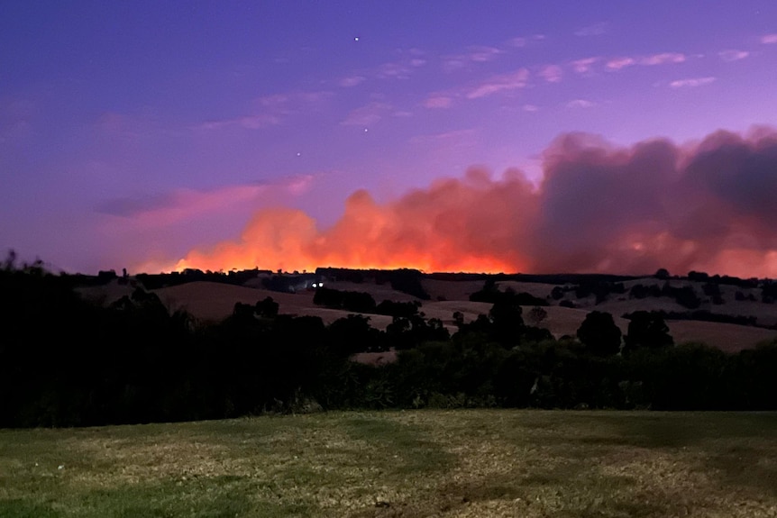 A fire and smoke lights up the horizon in a rural setting