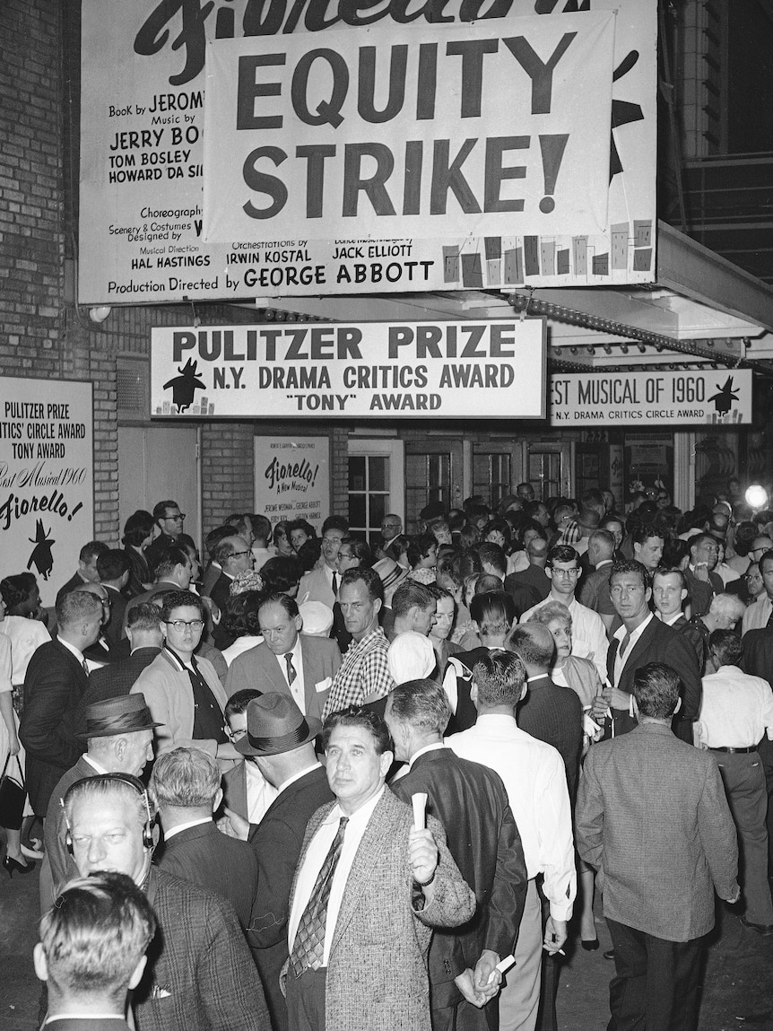 A black and white image of a crowd hanging outside a theatre.