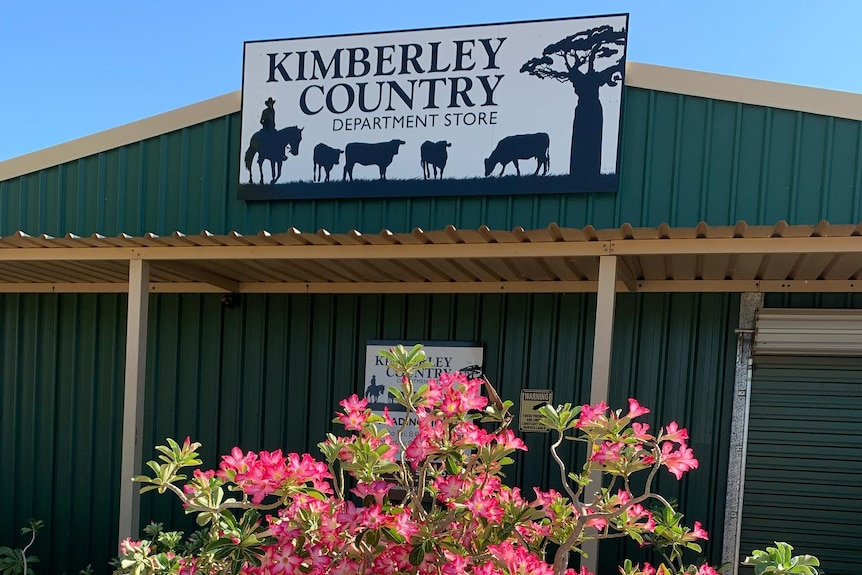 A store front with sign and pink flowers out front