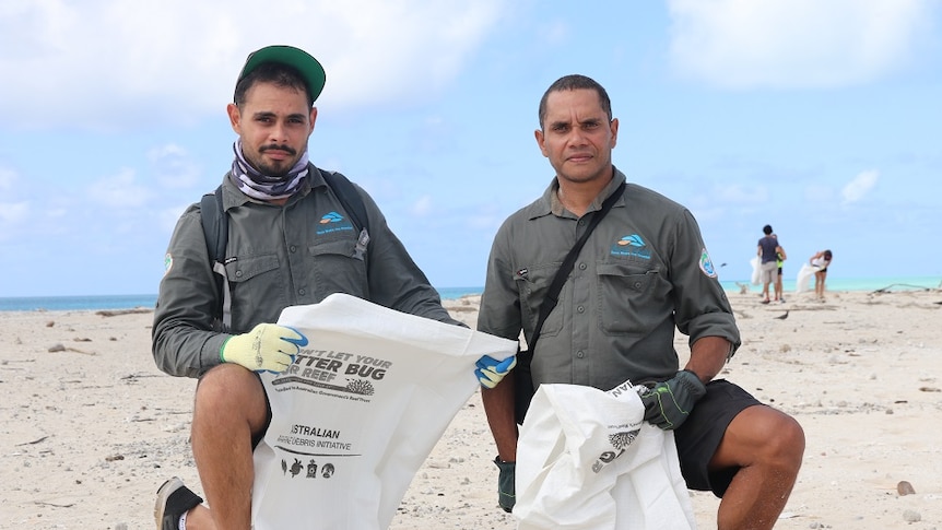 Two Indigenous rangers kneeling on the sandy island looking for rubbish.