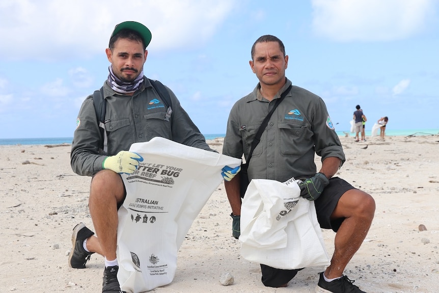 Two Indigenous rangers kneeling on the sandy island looking for rubbish.