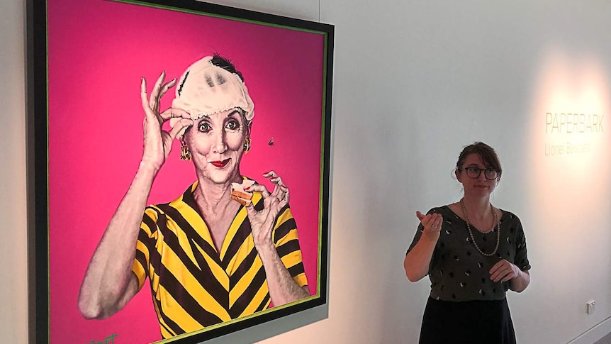 Deaf art tour guide Sigrid Macdonald signs in Auslan in front of an Archibald prize portrait