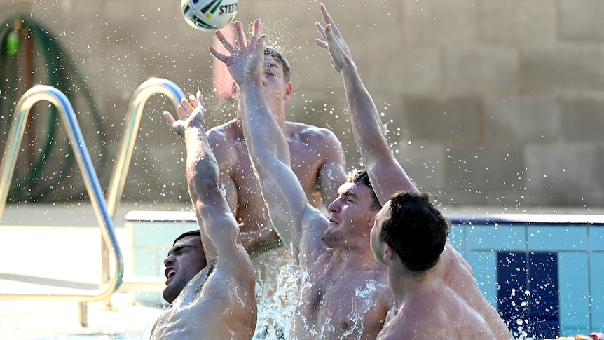 A group of NRL players stretch out of the water for a ball in the air as they do a recovery session in a swimming pool.sw 