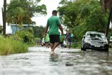 People walk through ankle-deep water along a road that runs between trees and under powerlines