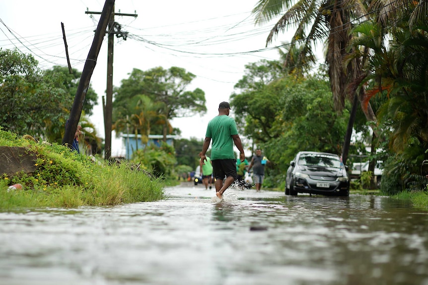 People walk through ankle-deep water along a road that runs between trees and under powerlines