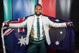 An man wearing a beige suit jacket and green pants with a green tie holds the Australia flag