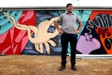 Jesse Zielke stands in front of a colourful street art mural.