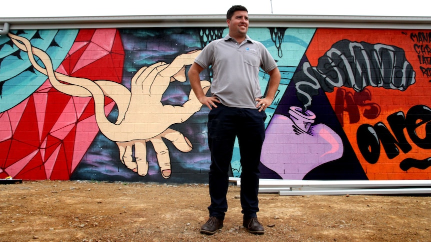 Jesse Zielke stands in front of a colourful street art mural.