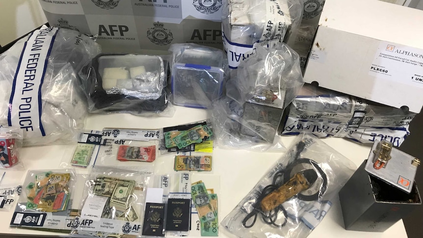 A table with federal police evidence bags containing Australian and US dollars, passports, and other parcels.