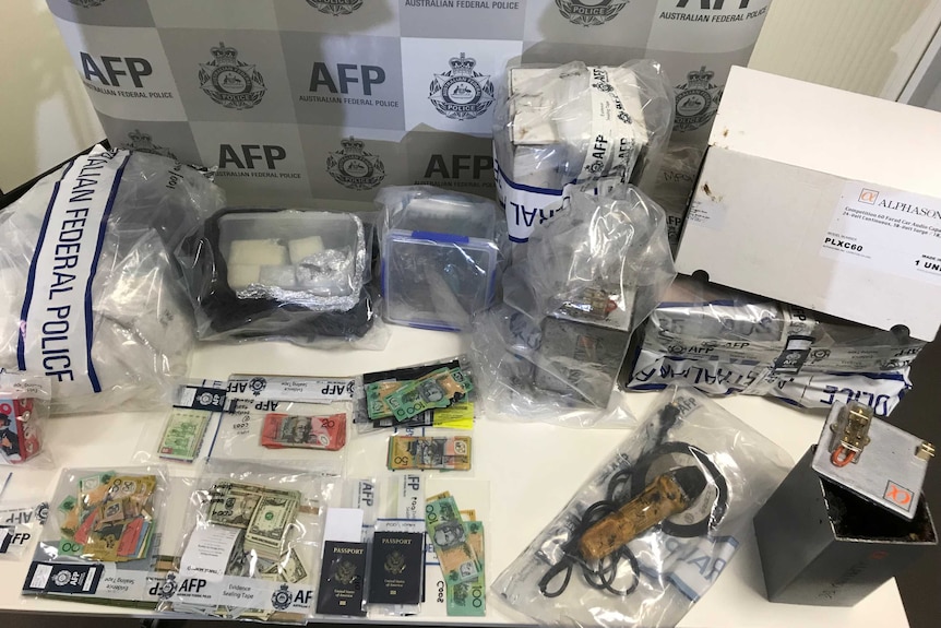 A table with federal police evidence bags containing Australian and US dollars, passports, and other parcels.