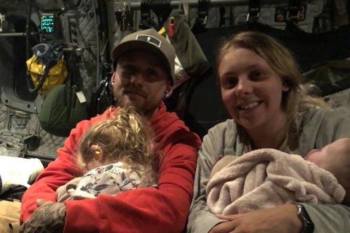 A man and woman hold their children on a military plane.